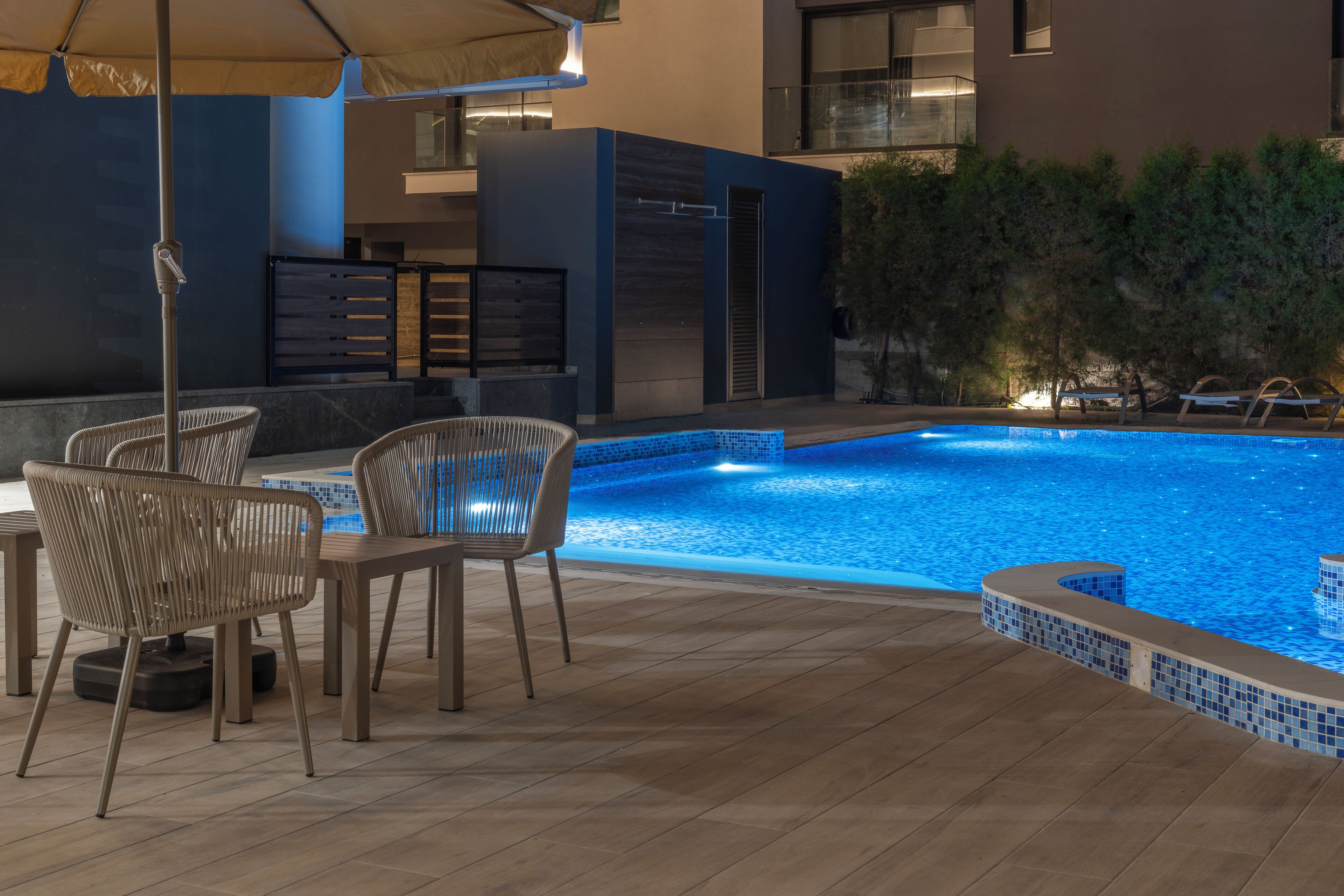 An outdoor pool area with a tiled edge, lounge chairs, and a table.
