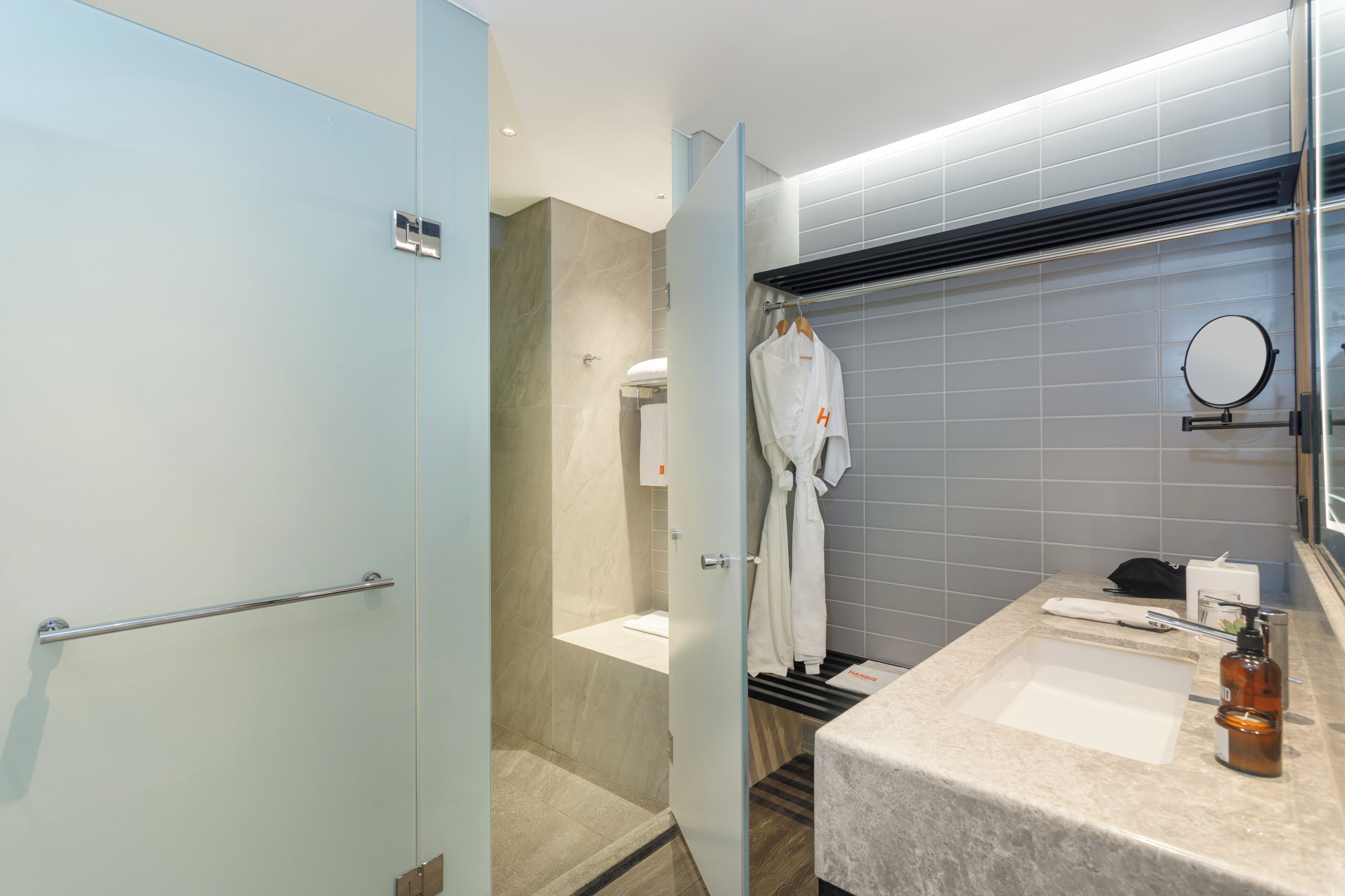 A modern bathroom with a shower, a sink with a mirror, and a robe hanging on a rack.