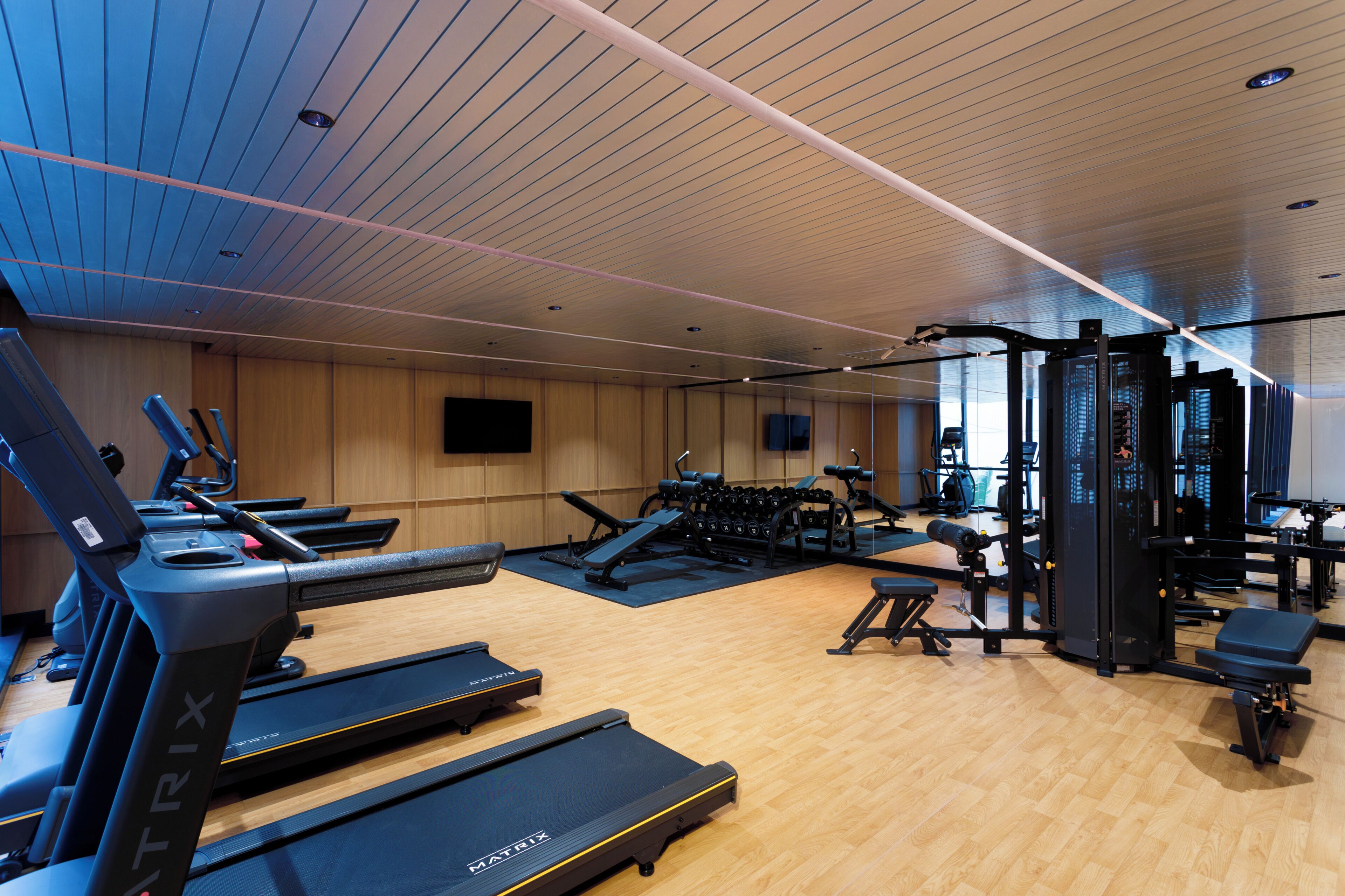 Une salle de sport équipée de tapis de course, d’appareils de musculation et d’un téléviseur fixé au mur.