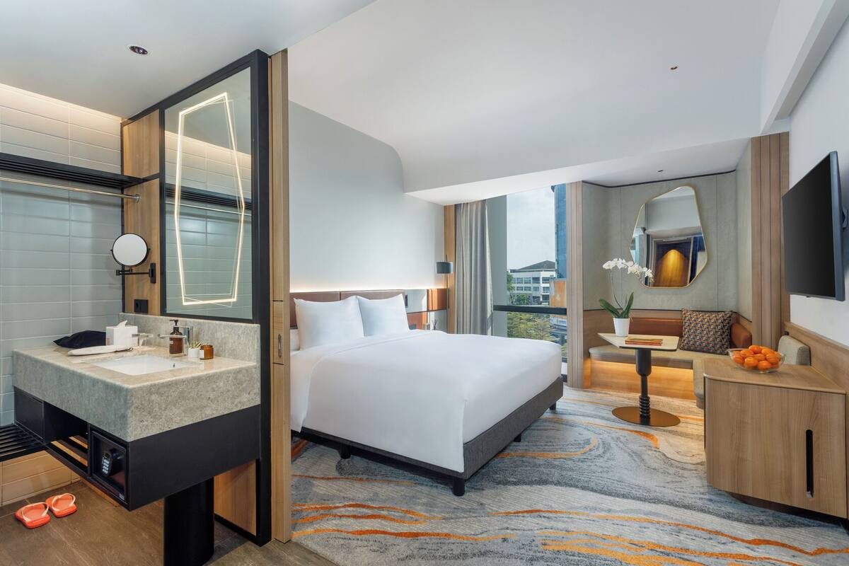 A modern hotel room with a large bed, a bathroom with a vanity, a desk, and a view of the city.