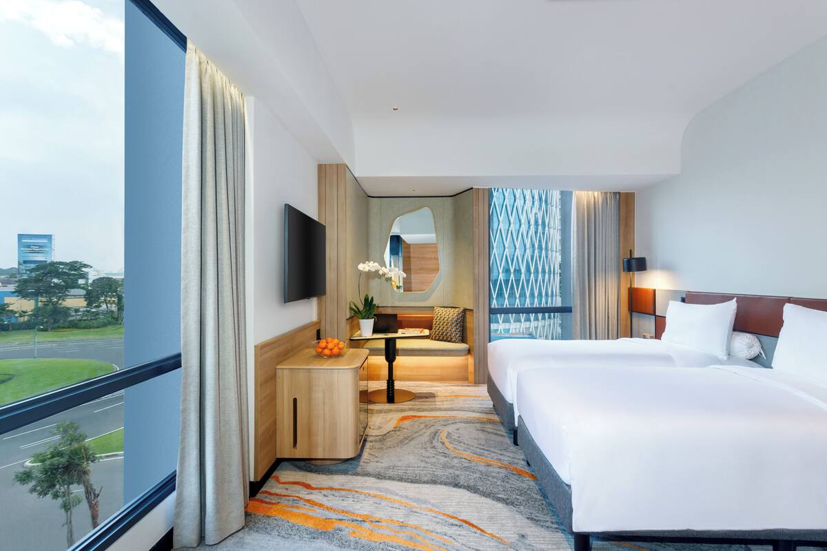 A hotel room with a large bed, a desk, a TV, and a view of the city.