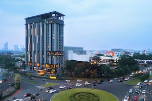 A multi-story building with a prominent vertical design, surrounded by a landscaped area with a circular design feature. - Harris Hotel & Convention Serpong (Gading Serpong)
