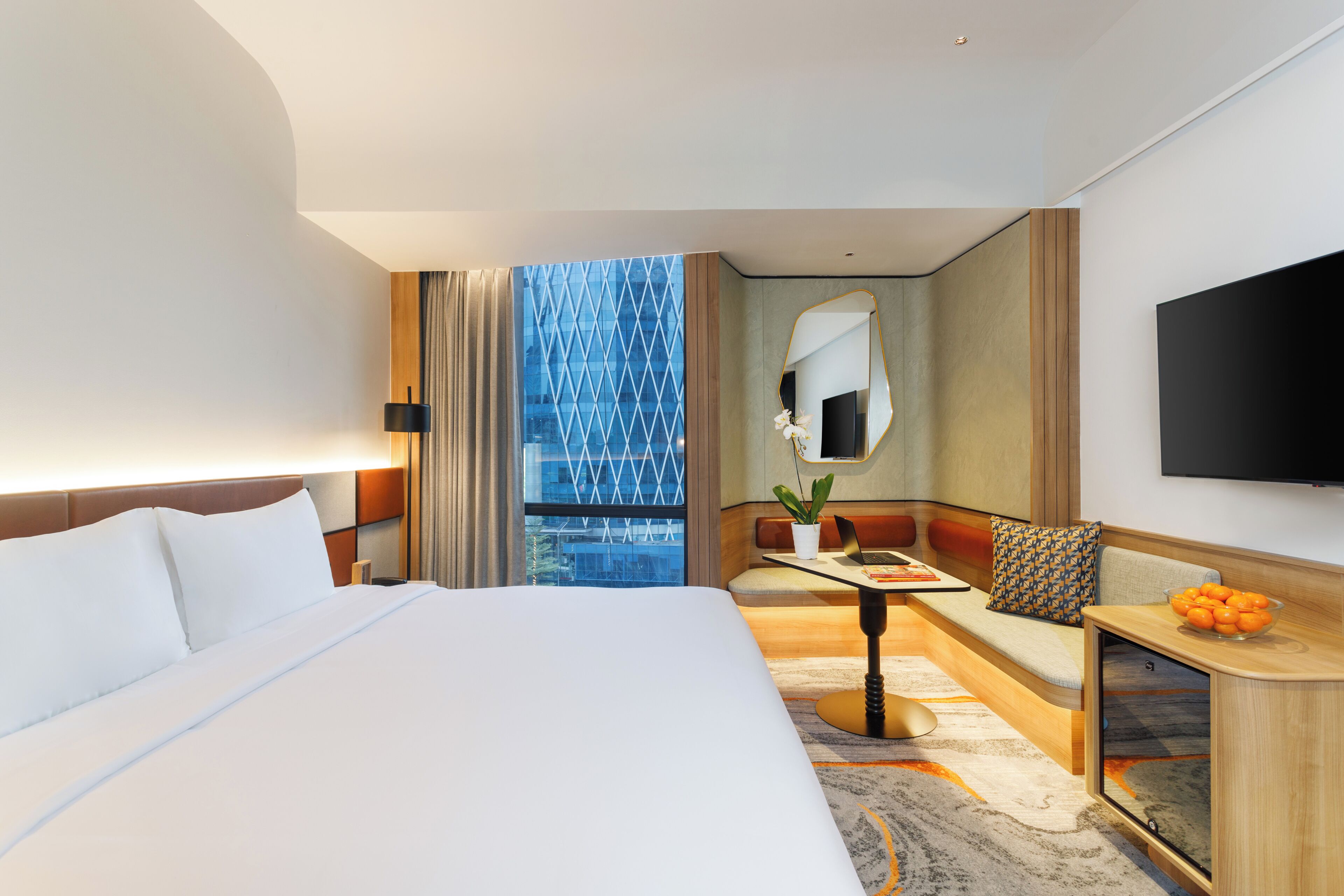 A hotel room with a large bed, a seating area with a table, a TV, and a view of a building.