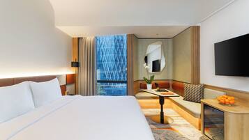 A hotel room with a large bed, a seating area with a table, a TV, and a view of a building.