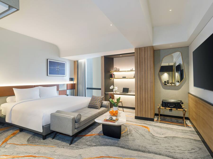 Une chambre d’hôtel moderne dotée d’un grand lit, d’un coin salon, d’un bureau et d’un grand miroir.