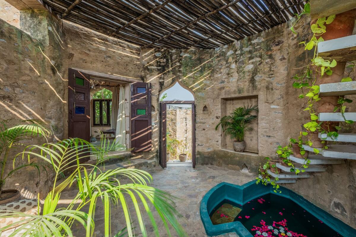 An interior courtyard with stone walls, a hanging chair, potted plants, and a water feature.