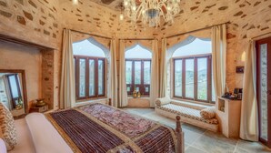 A room with a large bed, a chandelier, and three large windows with curtains. - Raht Manmatha (Udaipur)