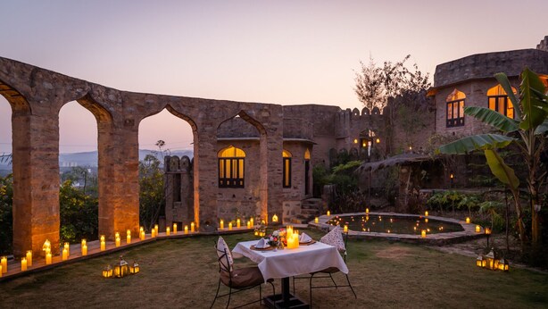 An outdoor dining area with a table set for two, surrounded by stone arches and candle-lit pathways. - Raht Manmatha (Udaipur)