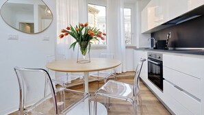 A modern kitchen with white cabinets, a black stove, and a glass vase with tulips on a round table. - FlaviaDesign City Suites Rome by Halldis (Rome)