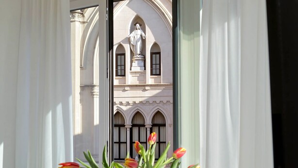 A view through a window with white curtains, revealing a building with arched windows and a statue. - FlaviaDesign City Suites Rome by Halldis (Rome)
