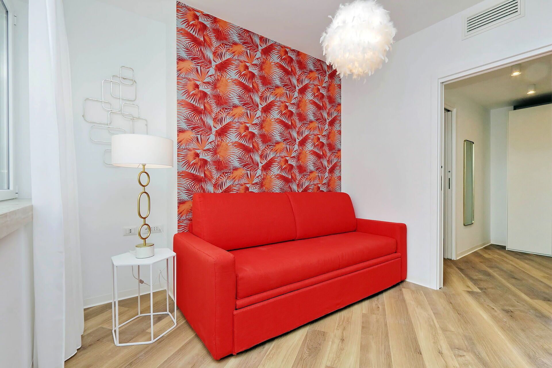 A red sofa, a white lamp, and a wall with a tropical leaf pattern.