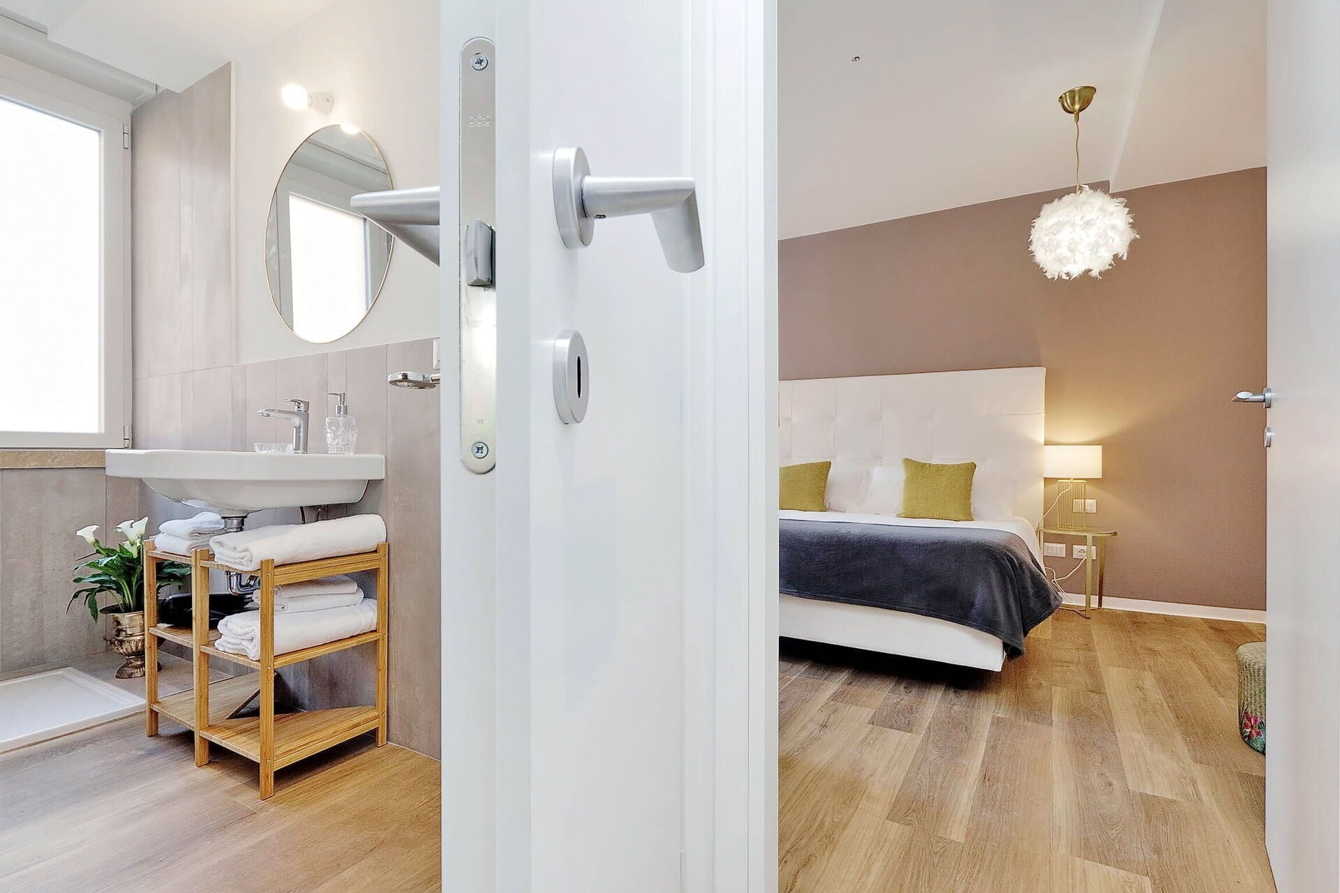 Een moderne badkamer met een wastafel, spiegel en handdoekrek. De kamer heeft houten vloeren en een groot raam.