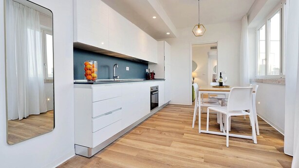 A modern kitchen with white cabinets, a wooden countertop, and a dining area with white chairs and a table. - FlaviaDesign City Suites Rome by Halldis (Rome)