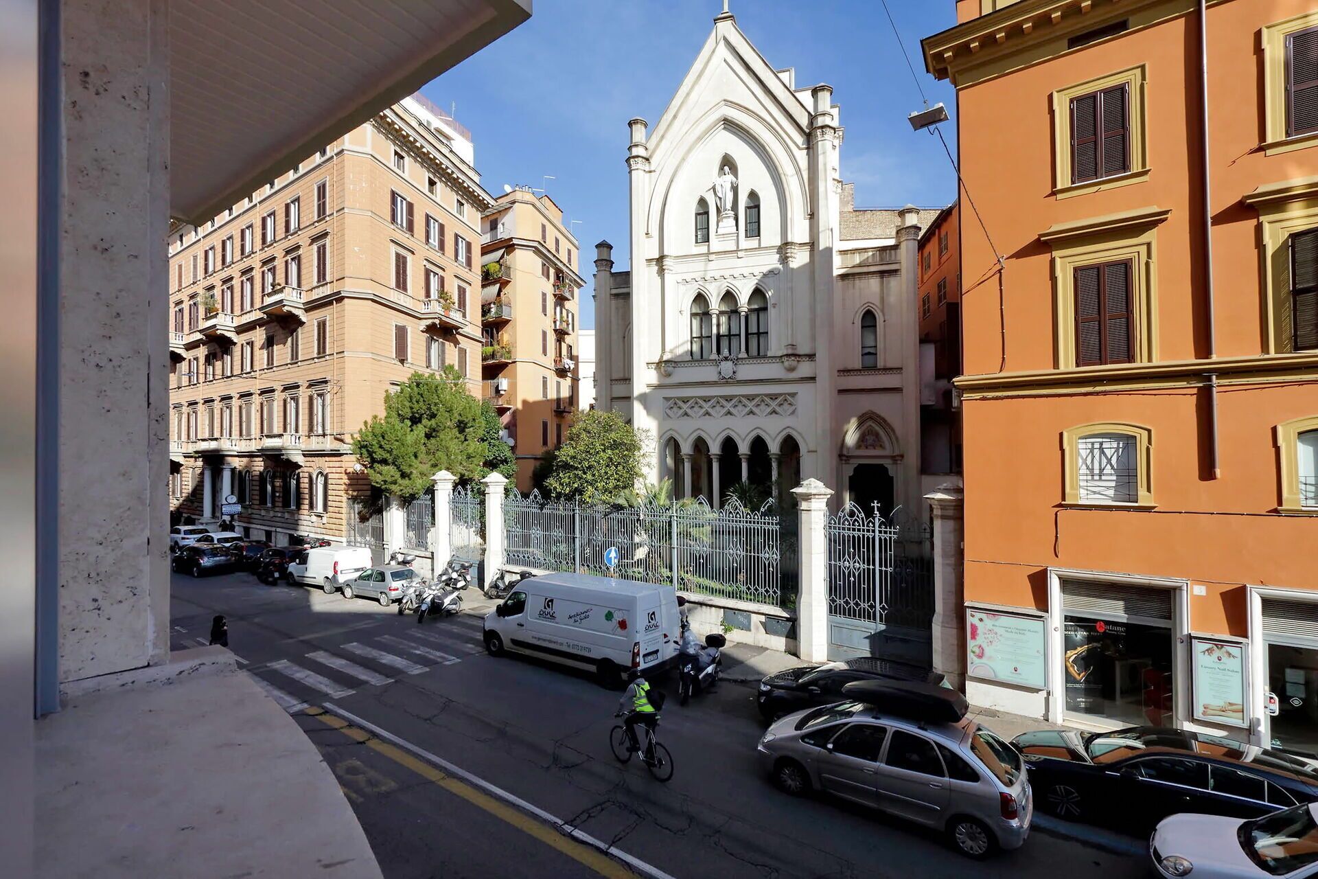 A street view with a building featuring a prominent Gothic-style archway and a statue.