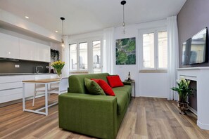 Moderni olohuone, jossa on vihreä sohva, pieni ruokapöytä ja keittiötila.