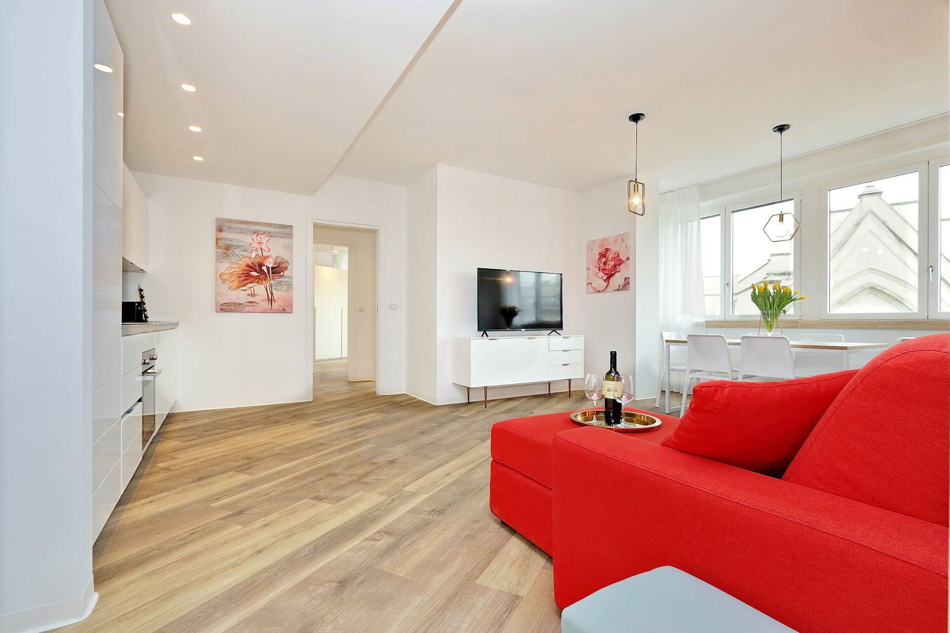 Una sala de estar moderna con un sofá rojo, un televisor y un comedor con mesa y sillas.