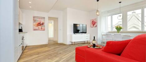 Una sala de estar moderna con un sofá rojo, un televisor y un comedor con mesa y sillas.