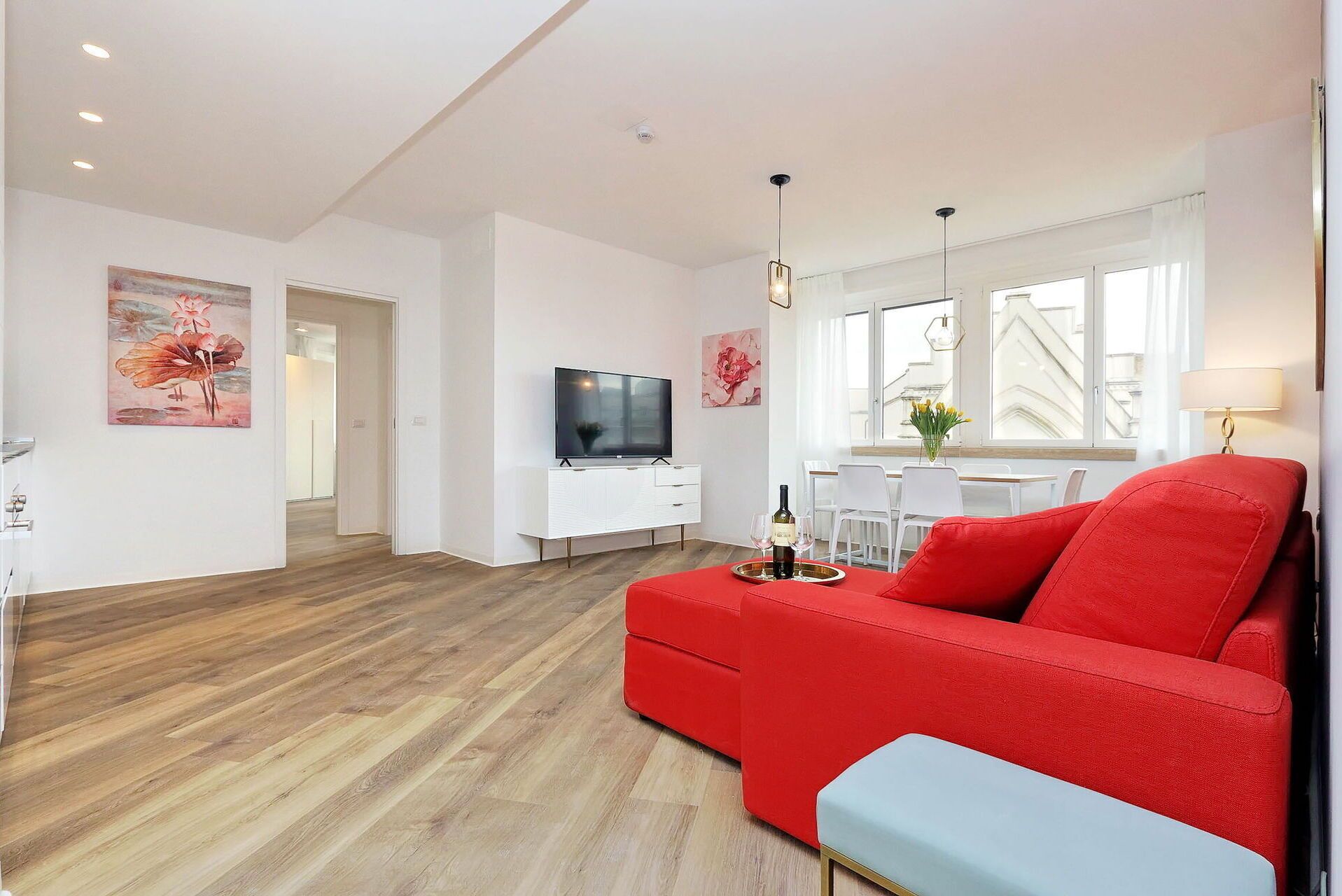 Una sala de estar moderna con un sofá rojo, un televisor y una zona de comedor con una mesa y sillas.