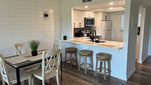 Una cocina moderna con armarios blancos, una isla central con taburetes y un comedor con sillas de madera y una mesa.