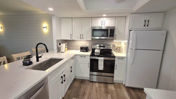 Una cocina moderna con armarios blancos, electrodomésticos de acero inoxidable y piso de madera.
