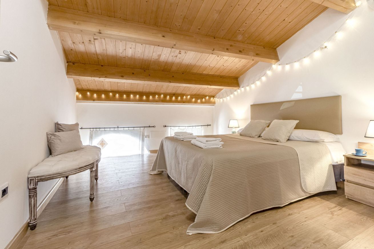 A bedroom with a large bed, a bench, and a wooden ceiling.