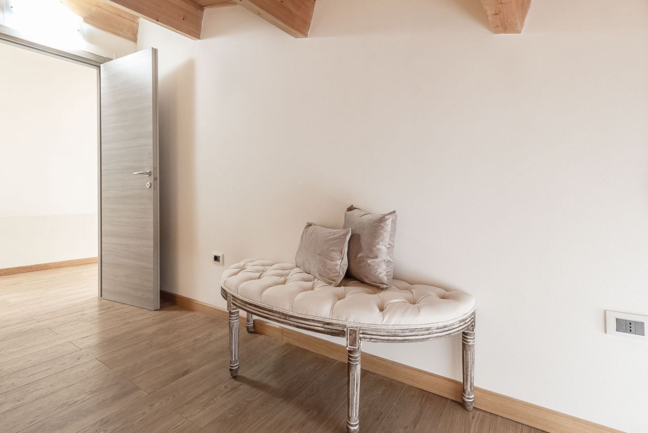 A room with a tufted sofa against a white wall, a wooden floor, and a door to the left.