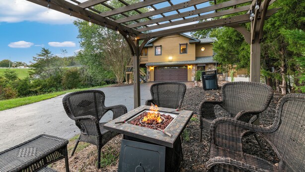 Un patio exterior con una chimenea, mobiliario de mimbre y una pérgola.