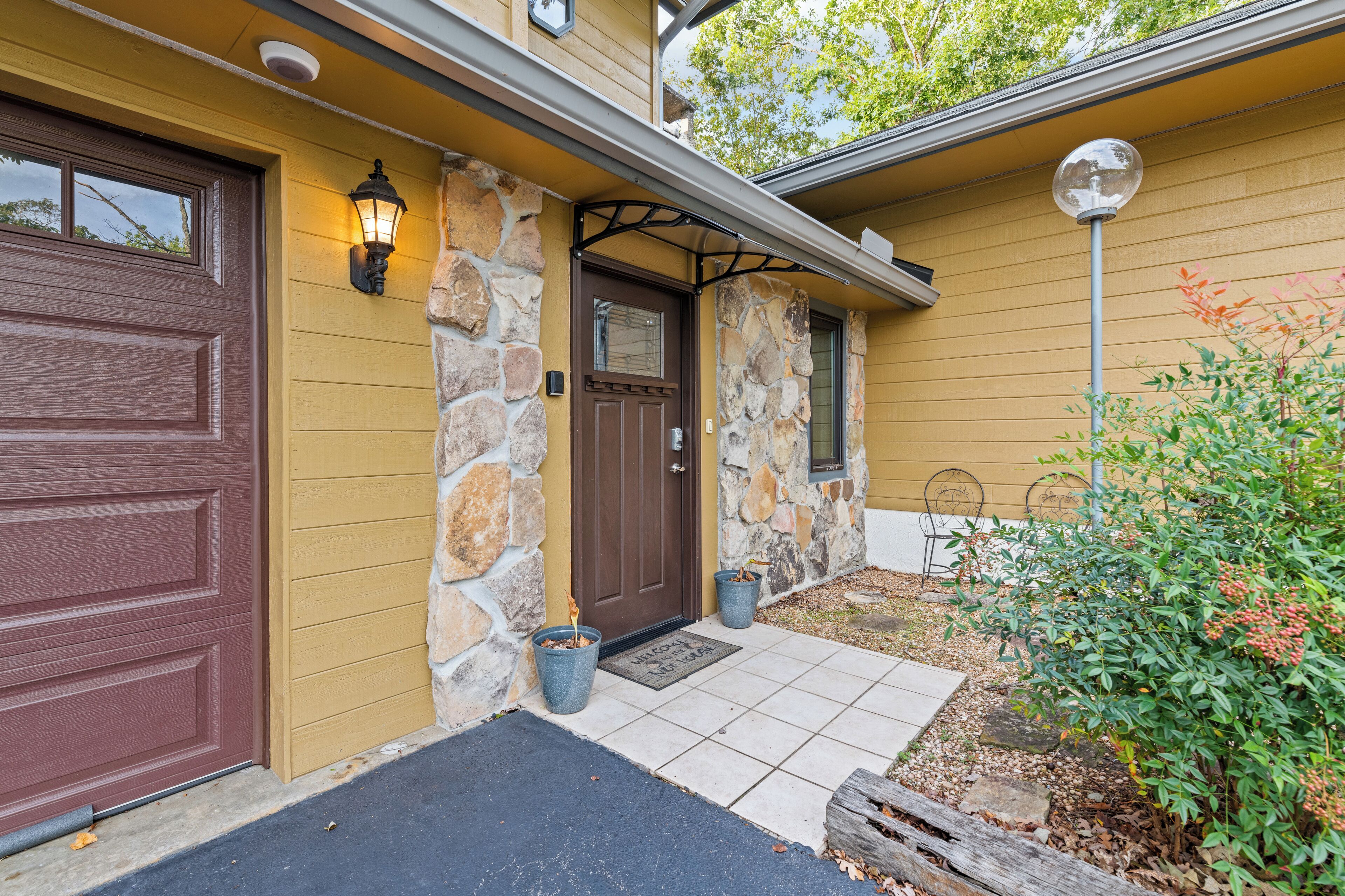 Une maison avec une porte de garage marron, une façade en pierre et un paillasson devant l’entrée.