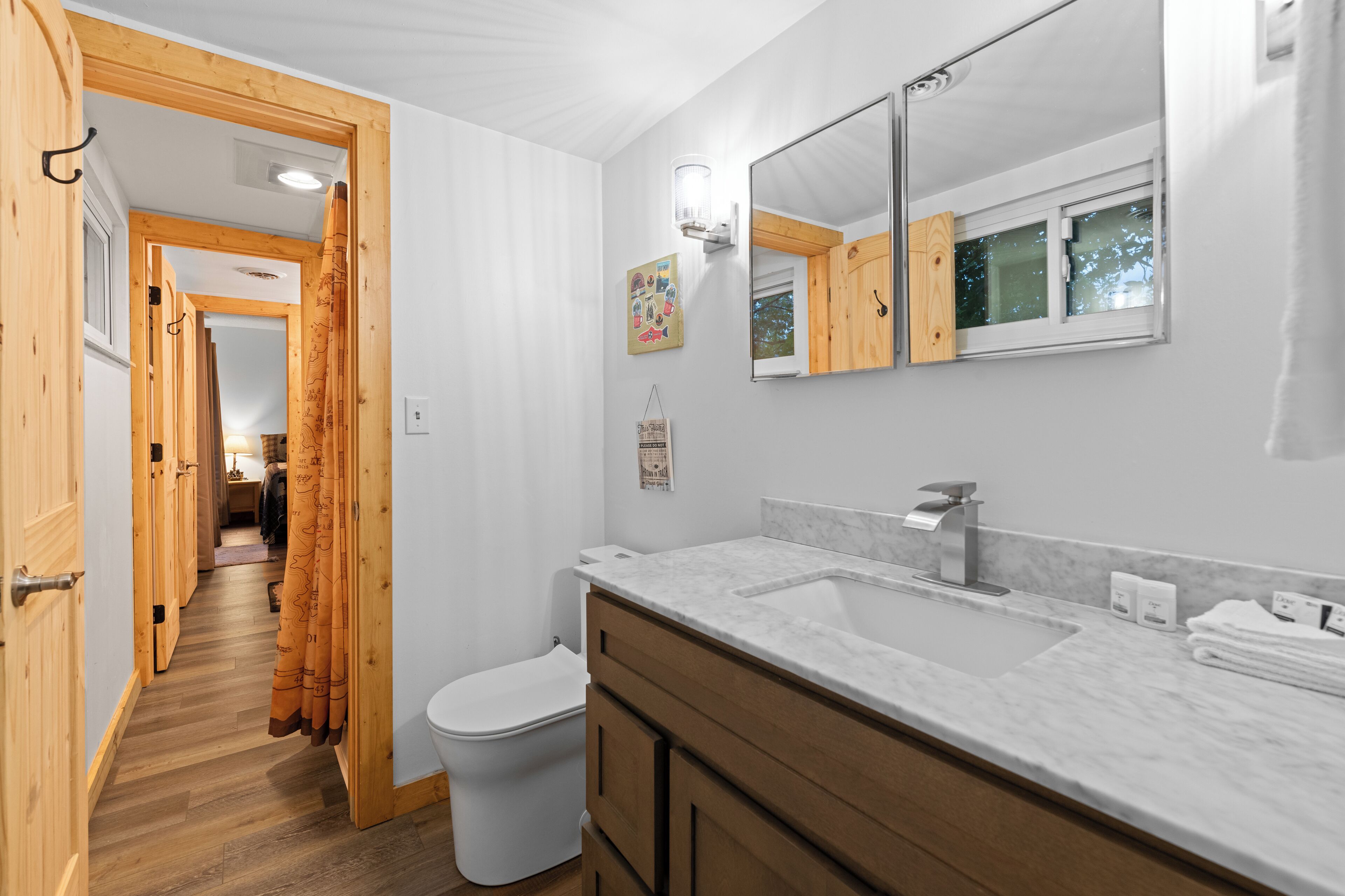 A bathroom with a white toilet, wooden cabinets, a marble sink, and a large mirror.