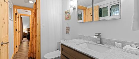 A bathroom with a white toilet, wooden cabinets, a marble sink, and a large mirror.