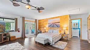 Un dormitorio espacioso con una cama grande, un escritorio y una silla, paredes de madera y vistas al exterior.