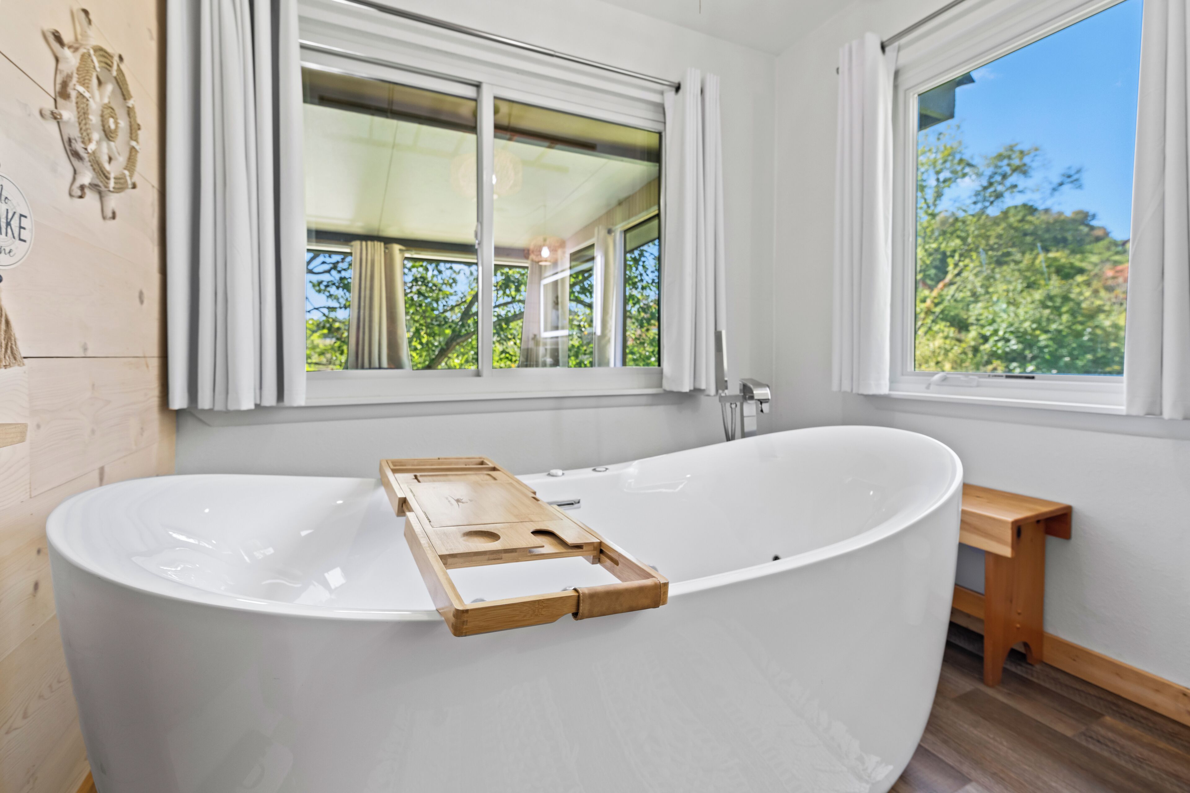 Un baño moderno con una bañera independiente, una mesita de madera y una ventana con vistas al verdor.