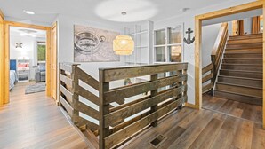 Un interior moderno con una escalera de madera, una isla central con una lámpara tejida y una obra de arte con temática náutica.