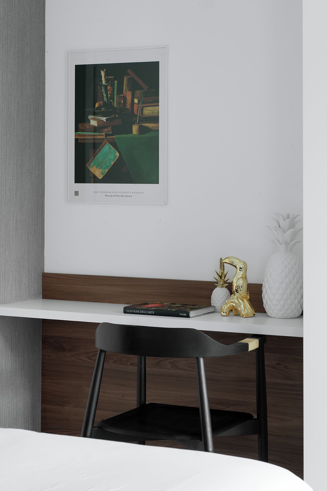 A modern room with a white desk, a framed artwork, a book, and a pineapple-shaped vase.