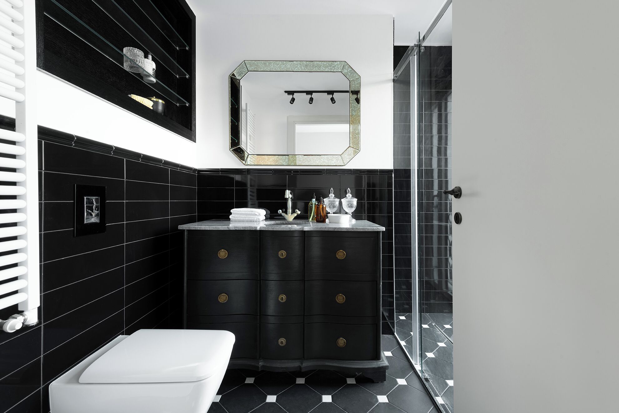 A modern bathroom with a black and white color scheme, featuring a black vanity with gold handles, a white toilet, and a glass shower enclosure.