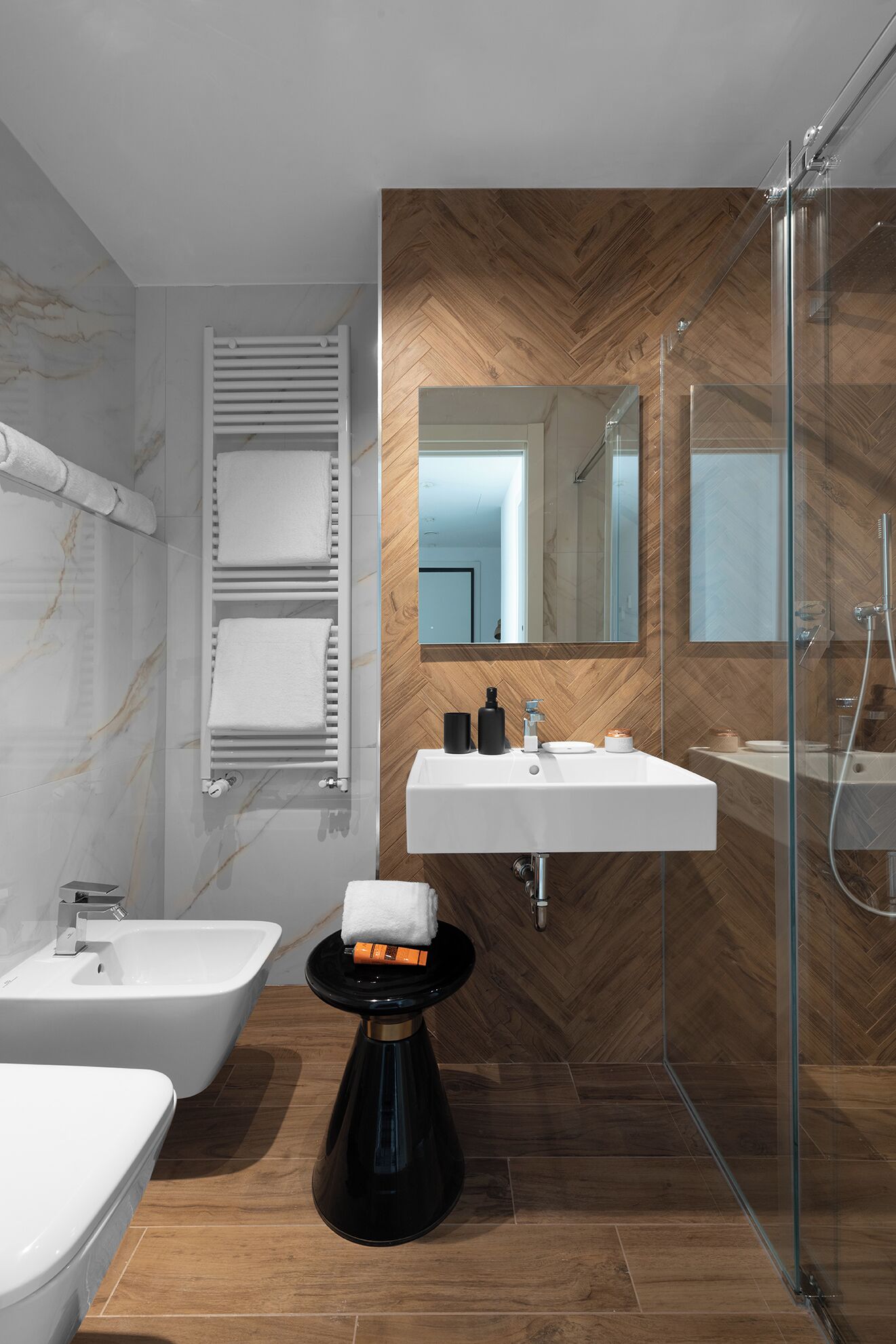 A modern bathroom with a bidet, a toilet, a sink, and a glass-enclosed shower.