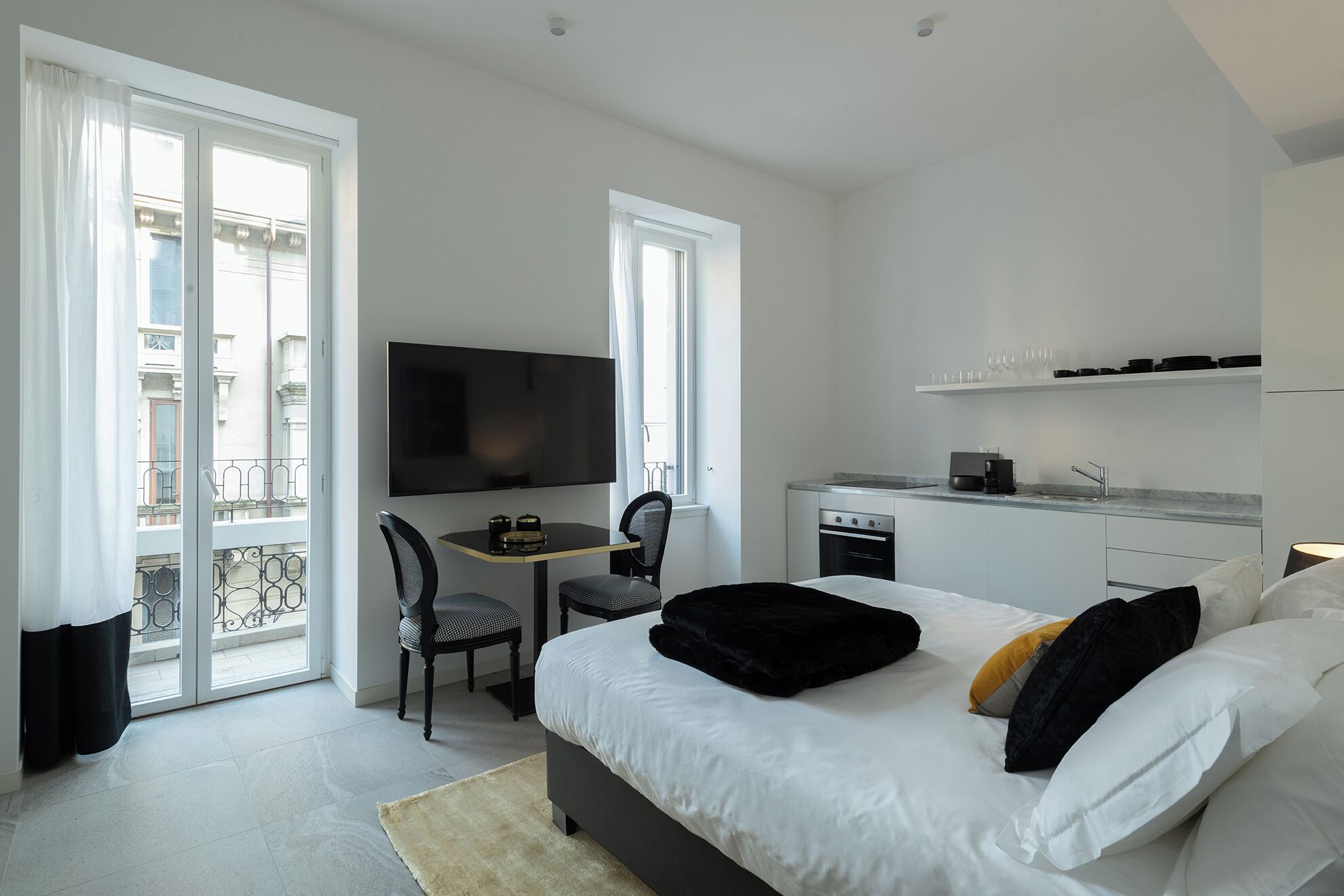 Ein modernes Hotelzimmer mit Bett, Fernseher, Essbereich und Küchenzeile.