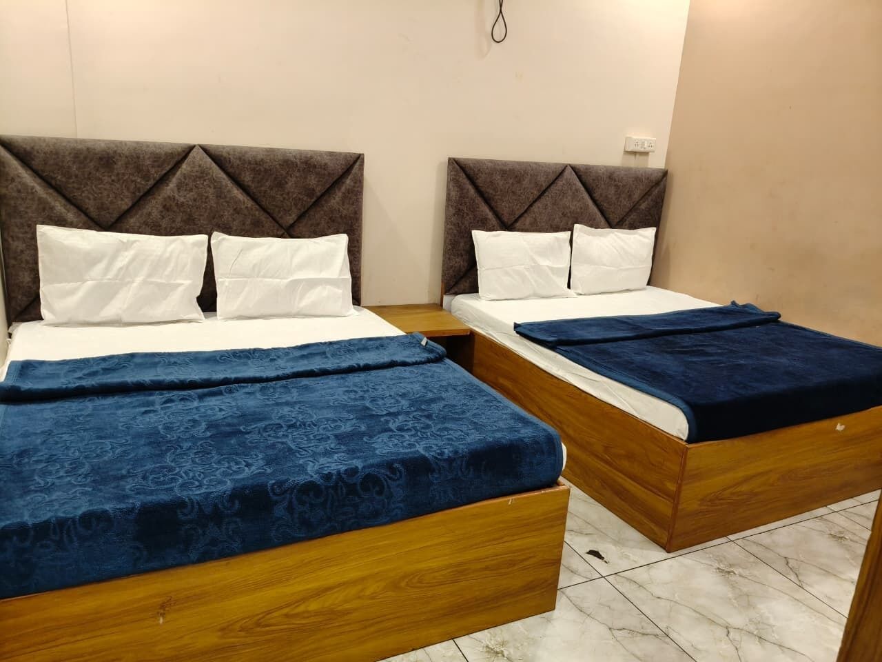 Two wooden beds with headboards, white pillows, and blue bedspreads in a room with tiled flooring.