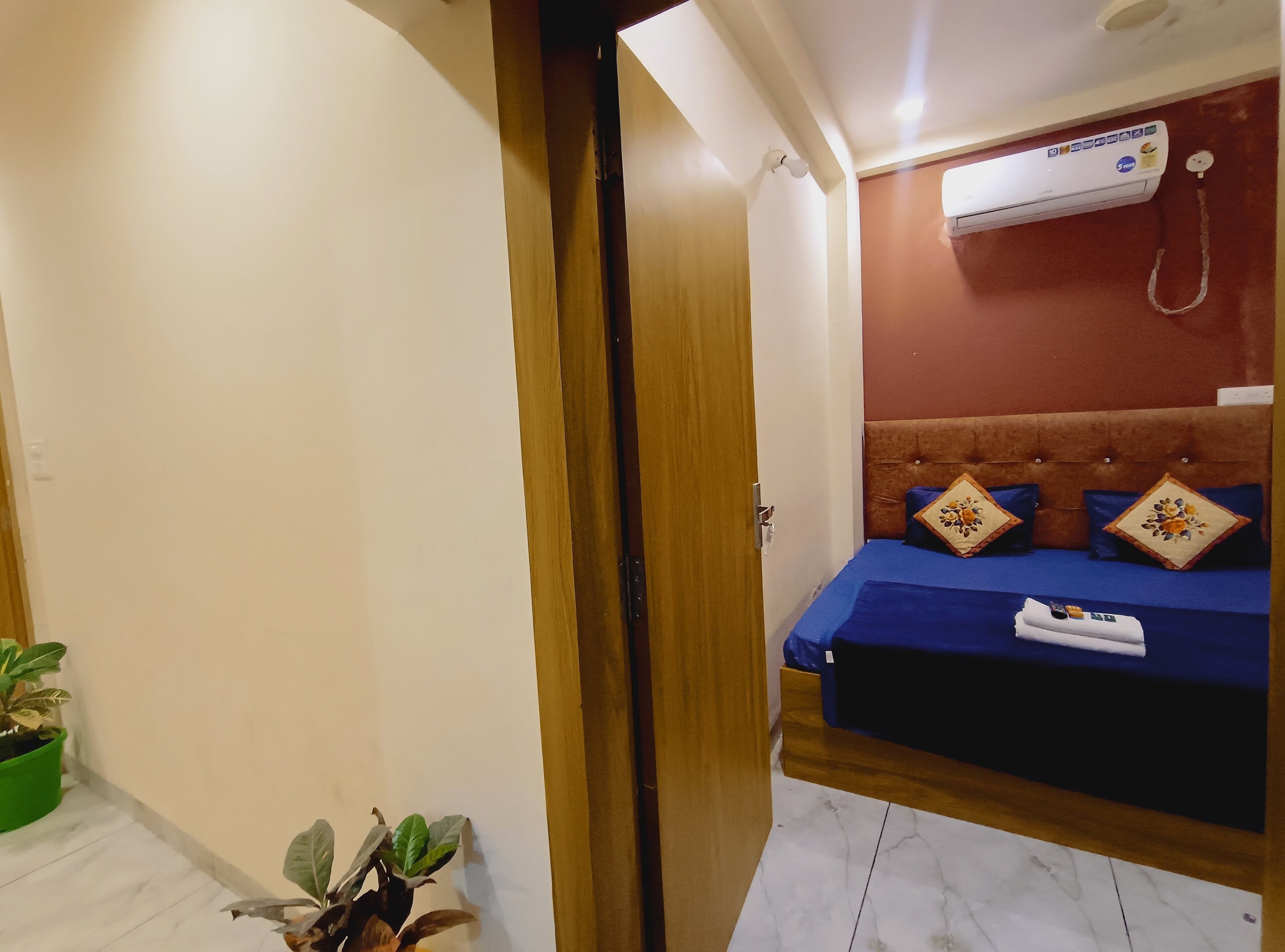 A bedroom with a bed, a wall-mounted air conditioner, and a potted plant.