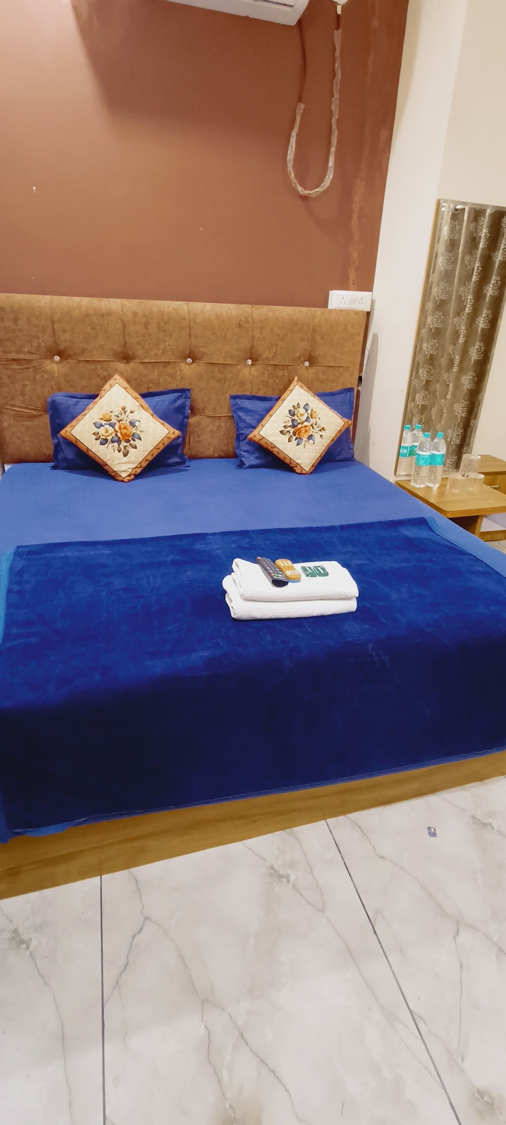 A neatly made bed with a blue bedspread, two decorative pillows, and a folded white towel on the bed.