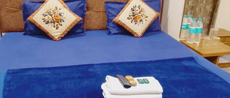 A neatly made bed with a blue bedspread, two decorative pillows, and a folded white towel on the bed.