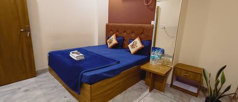 A hotel room with a bed, a nightstand, a mirror, a potted plant, and an air conditioning unit.