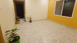 A room with a tiled floor, a window with blinds, and potted plants. - Hotel Laxmi villa (Ujjain)
