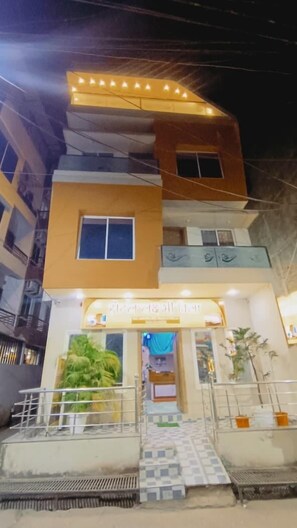 Un edificio de varios pisos con una entrada destacada, una escalera que lleva a la planta baja y un pequeño balcón en el nivel superior.
