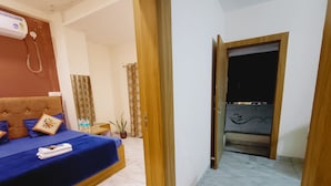 A hotel room with a bed, a small table with water bottles, a potted plant, and a bathroom visible through an open door. - Hotel Laxmi villa (Ujjain)