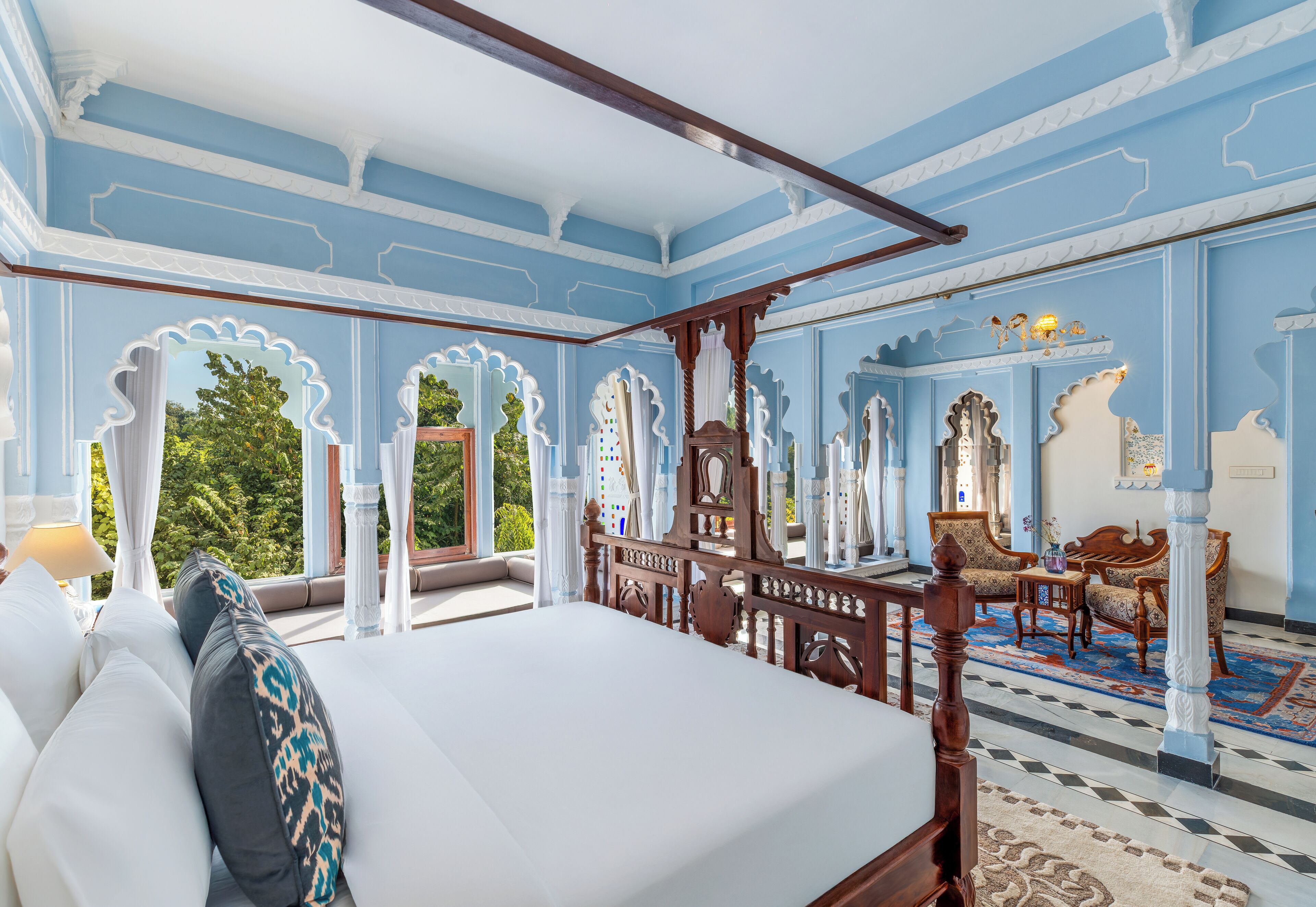 Une chambre à coucher avec un lit à baldaquin, un coin salon avec des fauteuils et une vue sur la verdure.