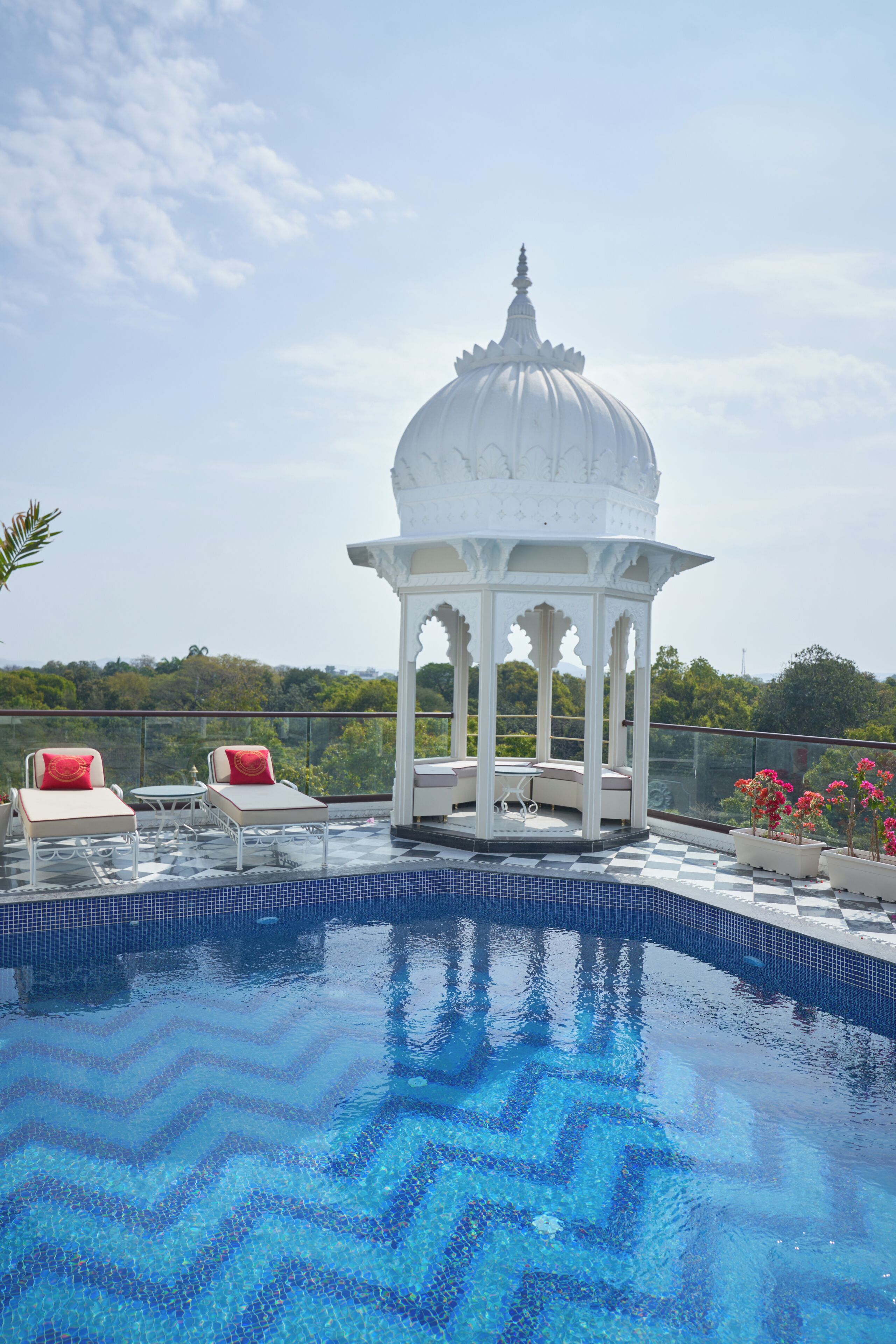 Una piscina con diseño a cuadros, un pabellón blanco y dos sillones de jardín con cojines rojos.