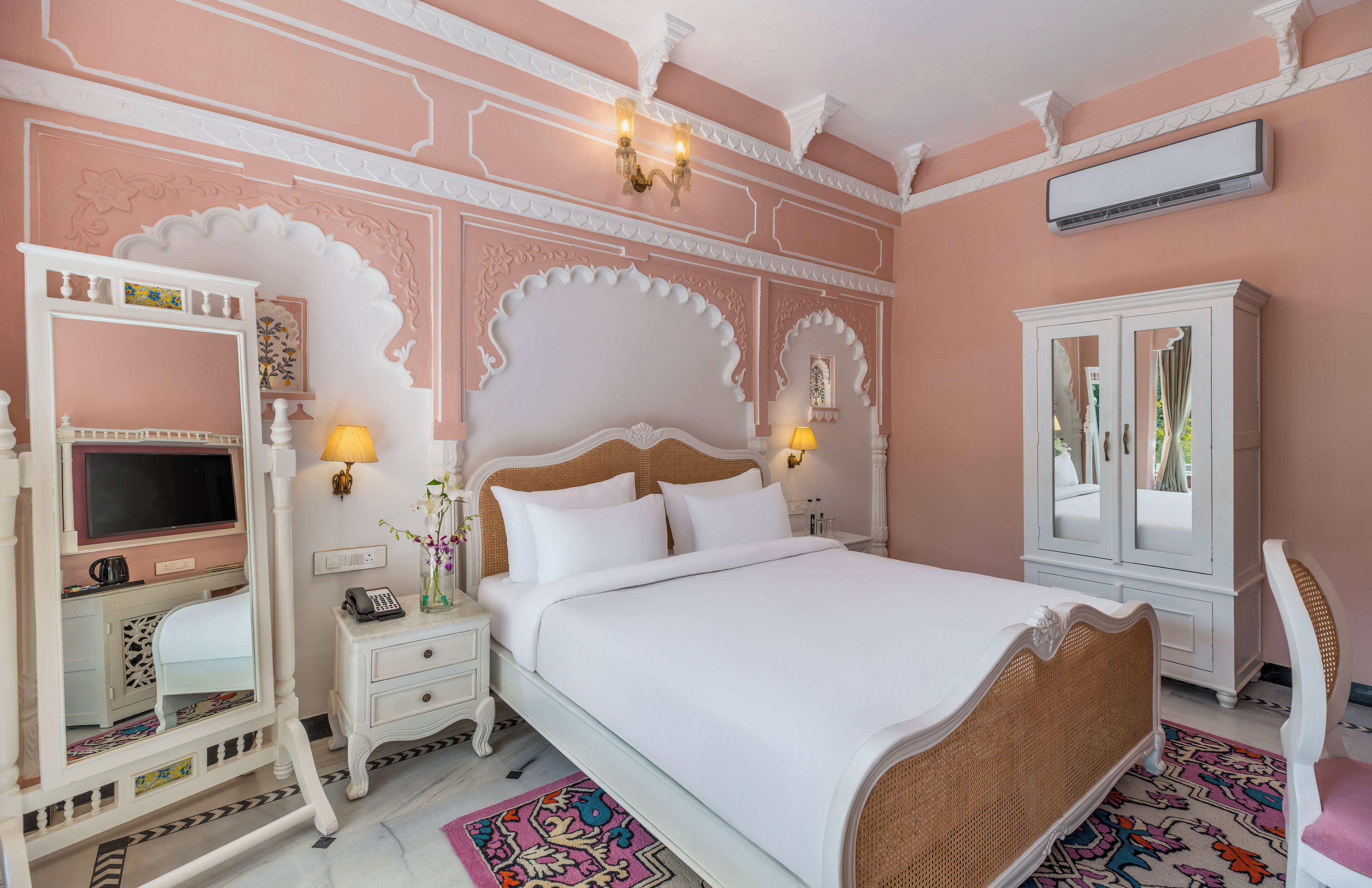 A bedroom with a large bed, a dresser, a vanity with a mirror, and a television.