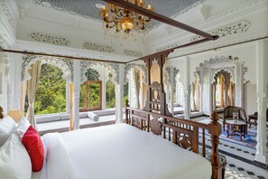 A luxurious bedroom with a large bed, ornate ceiling, and a view of greenery outside. - Oladar Haveli – My Downtown Hotels (Udaipur)