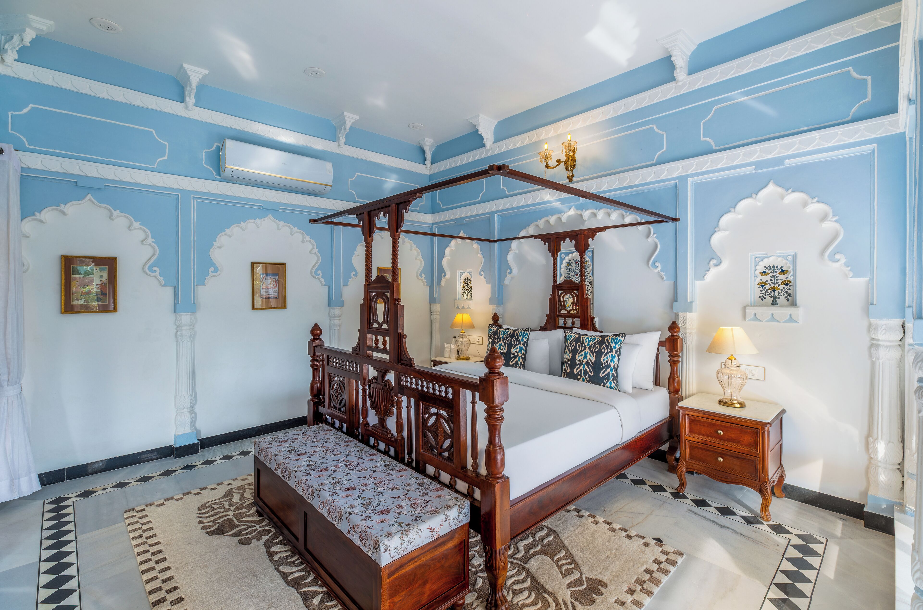 A bedroom with a four-poster bed, a bench, a nightstand, and a chandelier.
